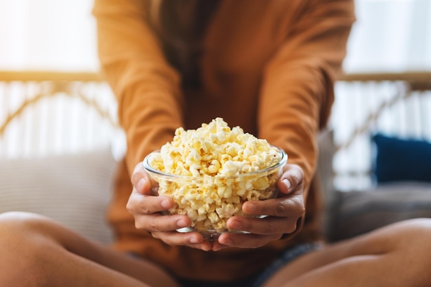 Gros plan image d'une femme tenant un bol de pop corn assis sur un canapé à la maison