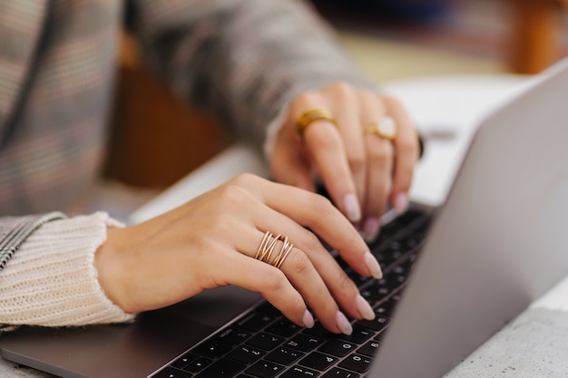 Gros plan image de mains de femme tapant et écrivant sur un ordinateur portable, travaillant au café.