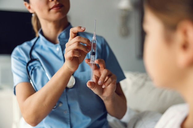 Gros plan de l'infirmière tenant la seringue avec cure et se prépare à donner un coup de feu à une fille malade