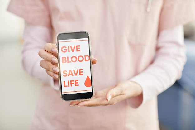 Gros plan sur une infirmière tenant un smartphone avec un slogan de sauvetage de sang au centre de don de sang