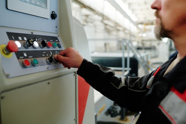 Gros plan d'un ingénieur en uniforme poussant des boutons sur la machine et contrôlant le travail en usine