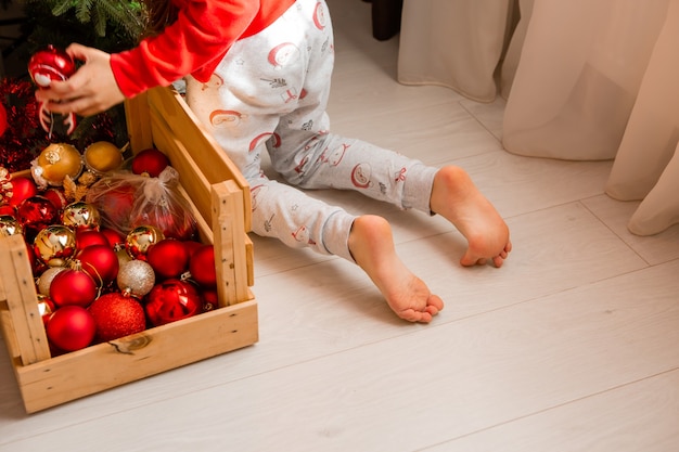 Gros plan sur les jambes d'un enfant en pantalon imprimé de Noël et pieds nus à genoux sur le sol