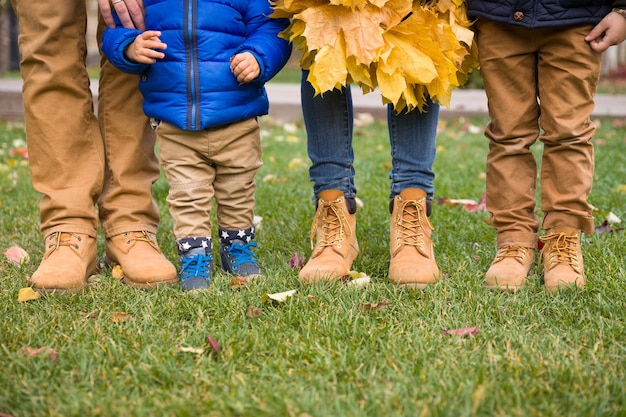 Gros plan des jambes d'une famille debout sur l'herbe verte et tenant des bouquets de feuilles de marple jaune