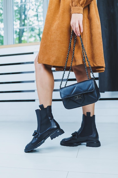 Gros plan des jambes féminines en chaussures à lacets en cuir noir Sac à main en cuir noir dans les mains des femmes Nouvelle collection automne de chaussures en cuir pour femmes 2022