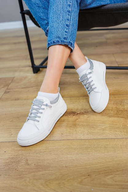 Gros plan des jambes féminines en jeans et baskets blanches décontractées Chaussures décontractées confortables pour femmes Baskets pour femmes en cuir blanc