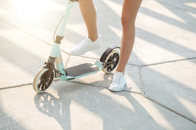 Gros plan des jambes de femme sur un scooter de coup de pied bleu sur route