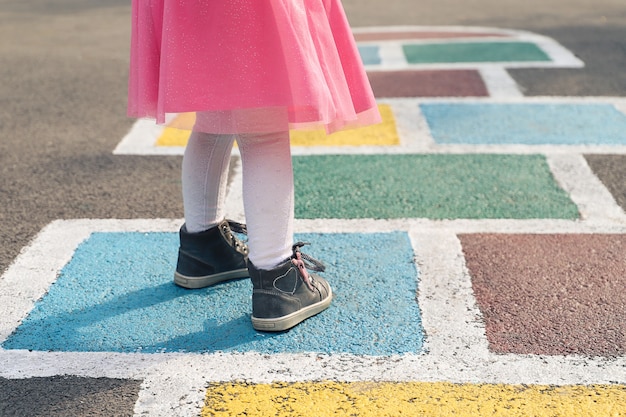 Gros plan des jambes des filles dans une robe rose et de la marelle dessinée sur l'asphalte Enfant jouant à la marelle