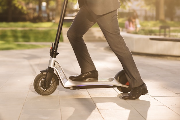 Gros plan sur des jambes homme en costume équitation scooter électrique en ville inconnu homme d'affaires en costume classique