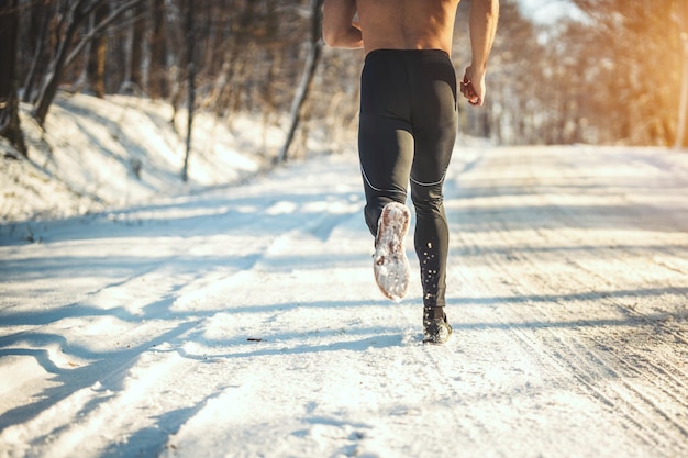 Gros plan sur les jambes d'un homme qui court sur la route forestière pendant l'entraînement hivernal à l'extérieur.