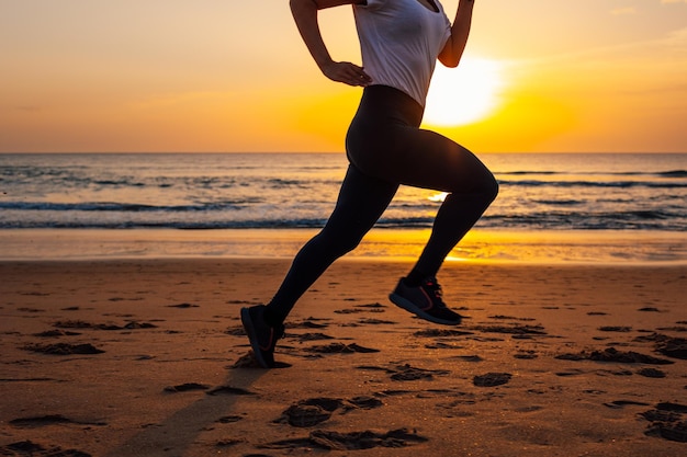 Gros plan sur les jambes d'une jeune femme méconnaissable s'entraînant au bord de la plage au coucher du soleil