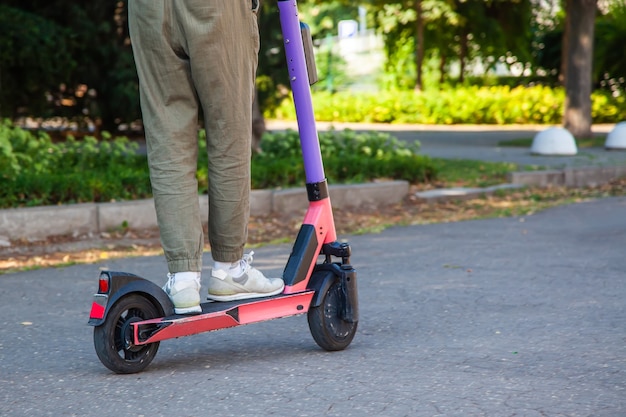 Gros plan sur les jambes d'un jeune homme sur un scooter électronique sur fond d'asphalte dans le parc de la ville