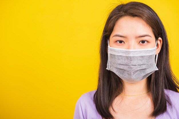 Gros plan sur une jeune adolescente asiatique portant un masque protecteur contre le coronavirus, le virus COVID-19 ou la poussière de filtre pm2,5 et la pollution de l'air, elle regarde un studio de caméra tourné sur fond jaune isolé