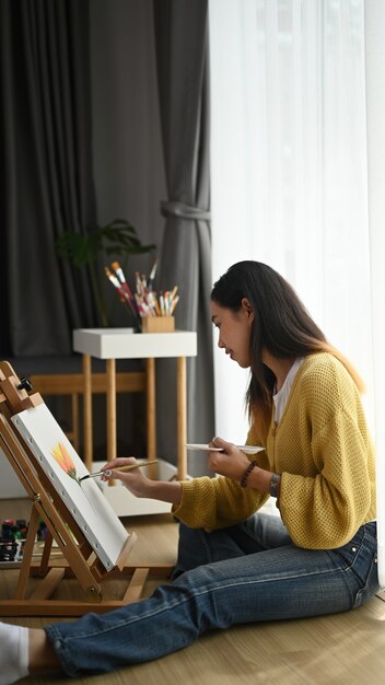 Gros plan d'une jeune artiste féminine assise sur le sol tenant un tube de peinture et mélanger les couleurs