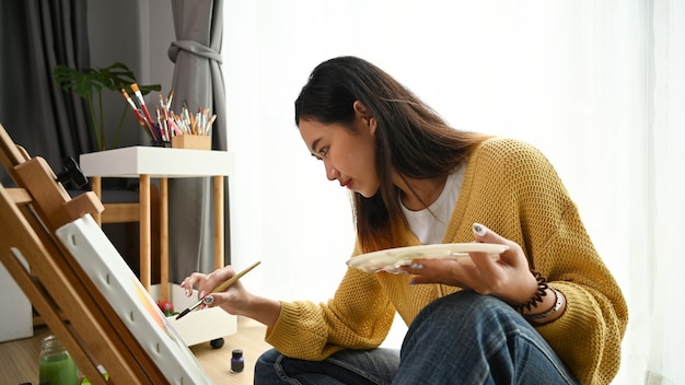 Gros plan d'une jeune artiste féminine assise sur le sol tenant un tube de peinture et mélanger les couleurs