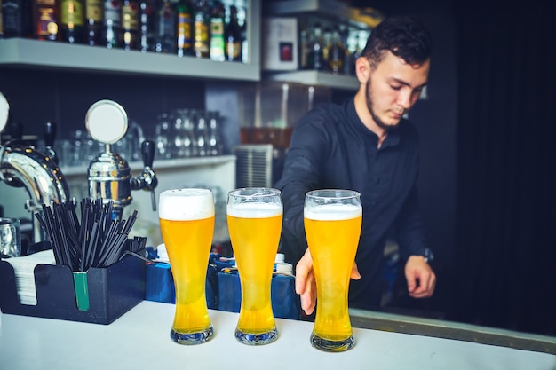 Gros plan sur un jeune barman versant de la bière en se tenant debout au comptoir du bar.