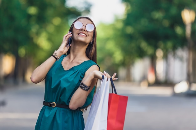 Gros plan, jeune, charmant, caucasien, cheveux, femme, à, sacs provisions, sourire, dents, et, parler téléphone