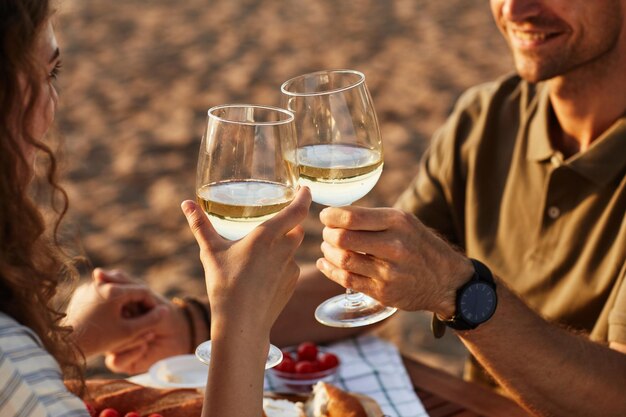 Gros plan d'un jeune couple buvant du vin à l'extérieur sur la plage tout en profitant d'un rendez-vous romantique au coucher du soleil copie...