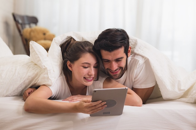 Gros plan jeune couple doux sur le lit, regarder quelque chose sur le gadget tablette, se détendre dans la chambre.