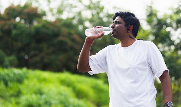 Gros plan sur un jeune coureur de sport asiatique, un homme noir porte des écouteurs d'athlète, il boit de l'eau d'une bouteille après avoir couru dans le parc de santé de la rue en plein air, concept d'exercice sain