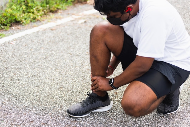 Gros plan sur un jeune coureur de sport asiatique, un homme noir porte des mains de montre, une articulation, une douleur à la jambe à cause d'une cheville tordue cassée lors de la course au parc de santé de la rue en plein air, un exercice sain