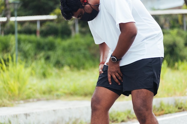 Gros plan sur un jeune coureur de sport asiatique homme noir porter des mains de montre joint tenir la jambe elle a des douleurs à la cuisse en courant dans le parc de santé de la rue en plein air, muscle de blessure d'exercice sain du concept d'entraînement