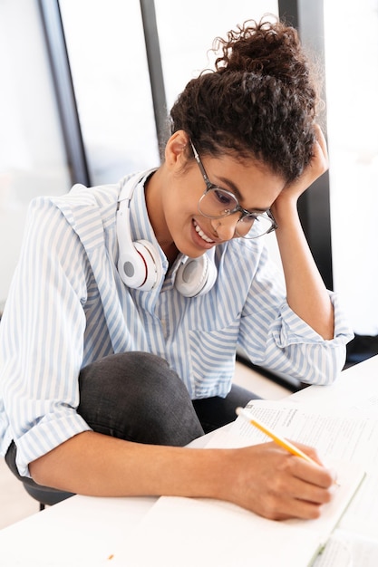 Gros plan d'une jeune femme africaine intelligente étudiant assis à table à la maison