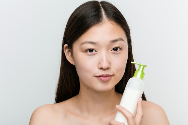 Gros plan d'une jeune femme asiatique belle et naturelle tenant une bouteille de crème hydratante