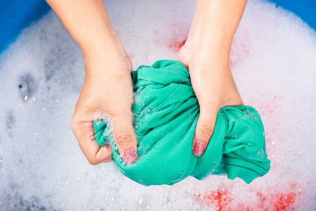 gros plan jeune femme asiatique utiliser les mains pour laver les vêtements de couleur dans le bassin