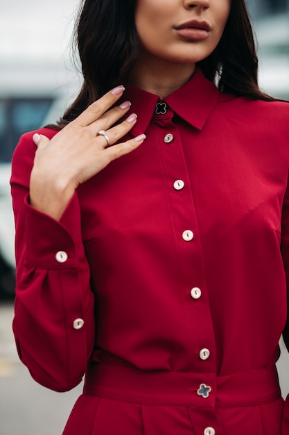 Gros plan d'une jeune femme assez élégante vêtue d'une robe rouge élégante en se tenant debout à l'extérieur. Concept de style et de mode