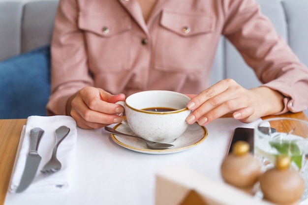 Gros plan sur une jeune femme assise à la table avec une boisson chaude, une cuillère, une fourchette, un couteau et une serviette au café