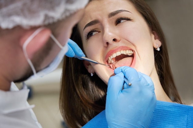 Gros plan d'une jeune femme ayant un contrôle dentaire en cabinet dentaire. Dentiste examinant les dents d'un patient avec des outils dentaires