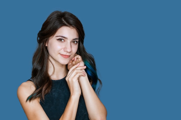 Gros plan d'une jeune femme brune élégante avec des mèches de cheveux bleus souriant sur fond bleu...