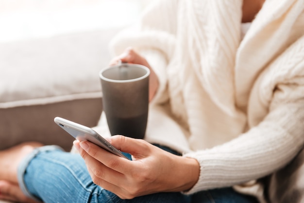 Gros plan d'une jeune femme buvant du café et utilisant un téléphone portable à la maison