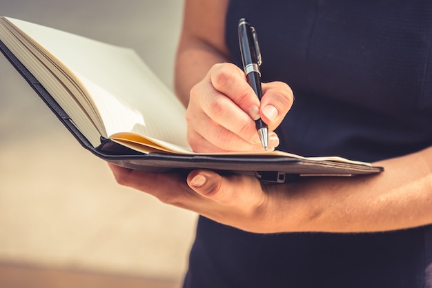 Gros plan de jeune femme écrivant des lettres dans le bloc-notes pour prendre note