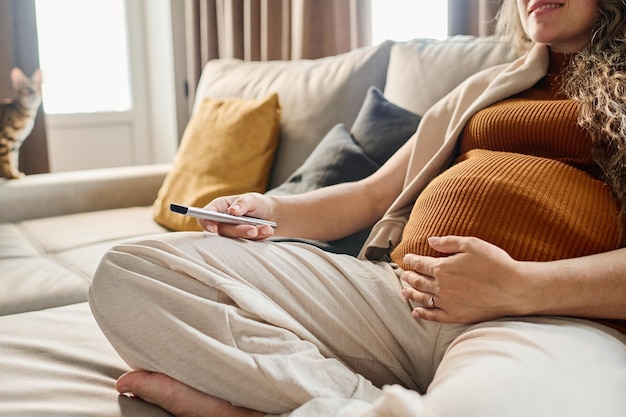 Gros plan d'une jeune femme enceinte en débardeur et pantalon choisissant une chaîne de télévision