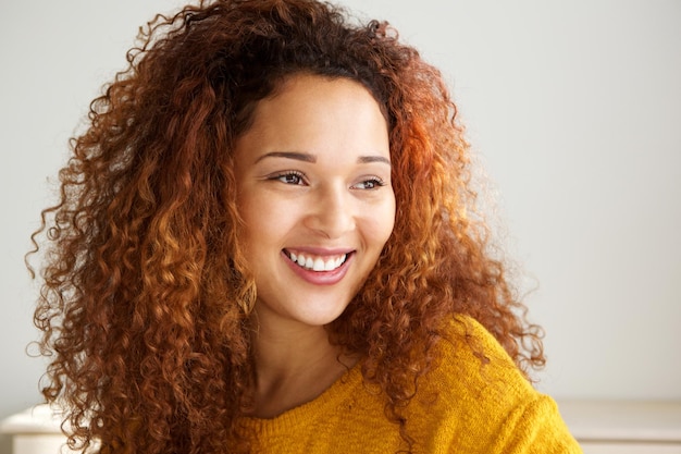 En gros plan, une jeune femme heureuse de race mixte souriant devant le mur blanc.