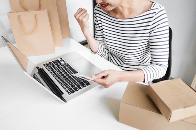 Gros plan d&#39;une jeune femme heureuse tenant une carte de crédit en saisissant les informations sur la carte tout en utilisant un ordinateur portable à la maison. Concept de magasinage en ligne.