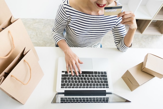 Gros plan de la jeune femme heureuse tenant la carte de crédit en saisissant les informations de la carte tout en utilisant un ordinateur portable à la maison. Concept de magasinage en ligne.