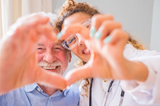 Gros plan sur une jeune femme médecin et un homme âgé montrant un signe cardiaque avec la main à la maison. Médecin aidant le patient âgé et prodiguant des soins. Soins médicaux aux personnes âgées.