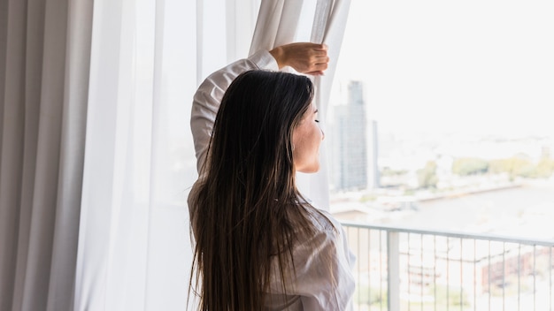 Gros plan, de, jeune femme, regarder dehors, par, balcon, de, rideau blanc