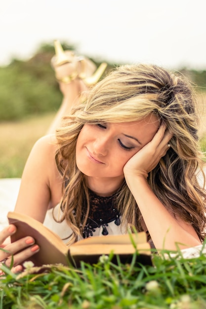 Gros plan d'une jeune femme romantique lisant un livre allongé sur l'herbe. Détendez-vous concept de temps en plein air.