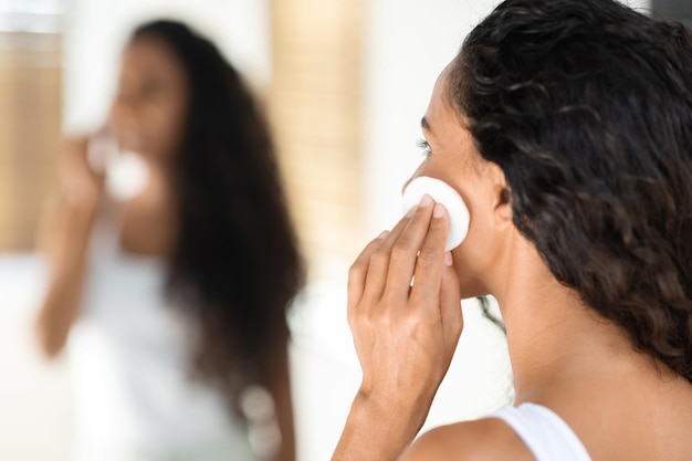 Gros plan d'une jeune femme séduisante nettoyant la peau avec un coton près du miroir