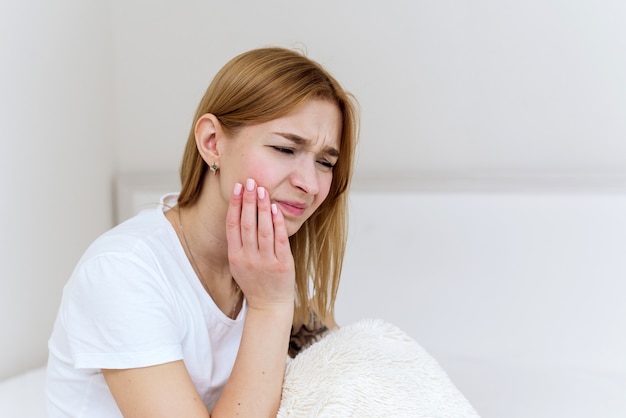 Gros Plan D'une Jeune Femme Souffrant De Maux De Dents Alors Qu'elle était Assise Dans Son Lit. Photo En Gros Plan D'un Homme Touchant Sa Joue Et Se Tordant Les Lèvres à Cause D'une Douleur Dentaire.