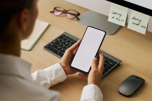 Gros plan jeune femme tenant un smartphone avec une maquette d'écran blanc sur le lieu de travail