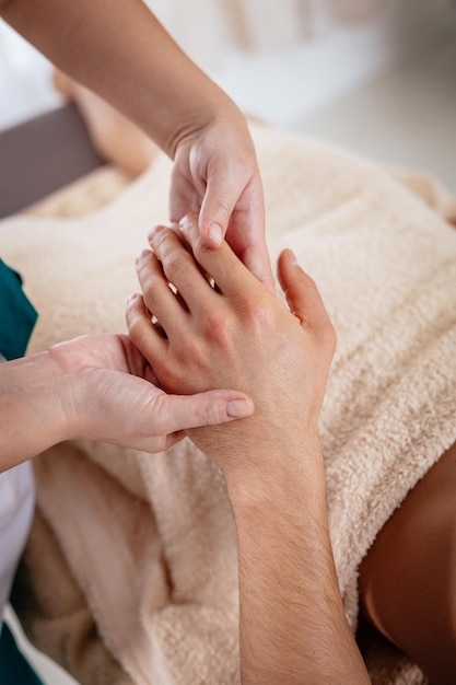 Gros plan d'une jeune femme thérapeute massant la main du jeune homme au salon de beauté.