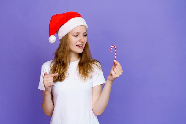 Gros plan d'une jeune fille blonde en bonnets de Noel et t-shirt blanc montre le doigt sur une sucette sous forme de ...