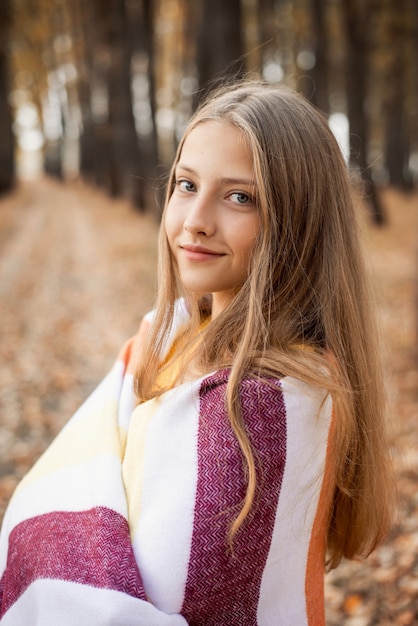 Gros plan d'une jeune fille blonde joyeuse couverte de plaid chaud à la recherche de l'appareil photo