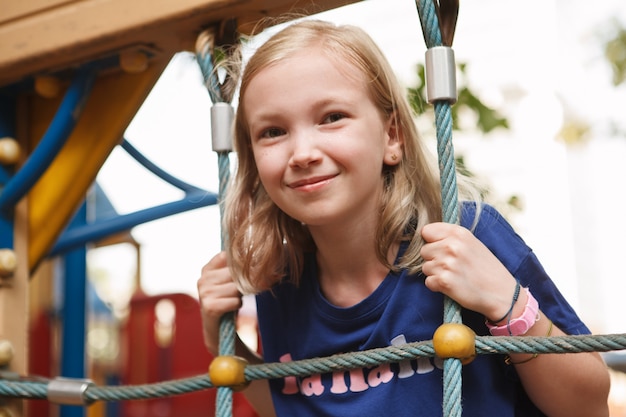 Gros plan d'une jeune fille joyeuse s'amusant à grimper au filet sur une aire de jeux