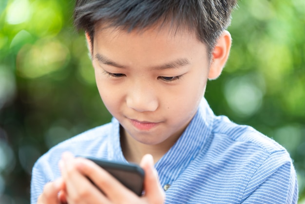 Photo gros plan jeune garçon asiatique à l'aide de téléphone portable dans le jardin