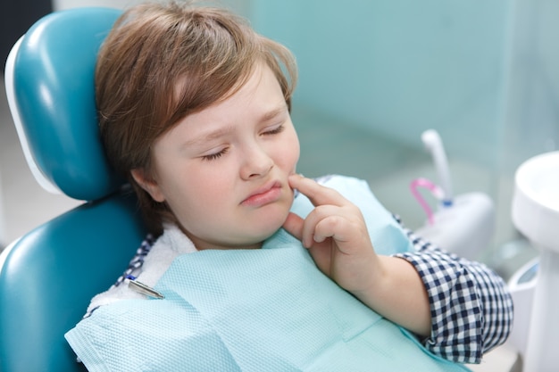 Gros plan d'un jeune garçon ayant mal aux dents, assis dans un fauteuil dentaire au bureau de dentistes